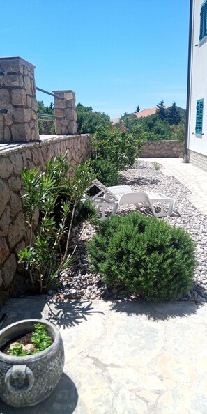 Een stenen muur, een kleine struik en een betonnen plantenbak met groen.