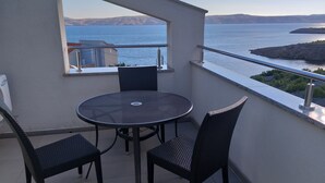 Uma varanda com uma mesa redonda e duas cadeiras, com vista para um corpo de água e uma terra distante.