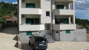 Um edifício com várias andares, varandas, uma escadaria e uma van estacionada.