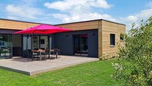 A modern house with a deck, a dining area, and a large red umbrella. - Bright new wooden house with enclosed garden 5 minutes from the beach (Gouville-sur-Mer)