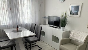 A modern living room with a dining table, chairs, a sofa, a TV, and a potted plant. - Cozy, quiet and central, a few meters to the beach, swimming pool in the house (Norderney)