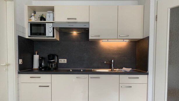 A compact kitchen with white cabinets, a microwave, a coffee maker, and a sink. - Cozy, quiet and central, a few meters to the beach, swimming pool in the house (Norderney)