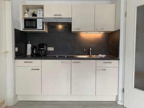 Una cucina compatta con mobili bianchi, un forno a microonde, una macchina da caffè e un lavandino.