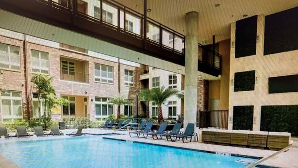 An indoor swimming pool with lounge chairs and a covered walkway. - High Rise Condo/Apartment in the Medical Center Area (Houston)