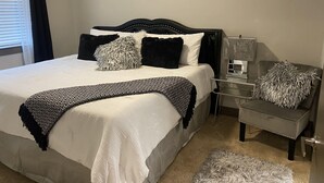 A neatly arranged bedroom with a bed, bedside table, and a mirror on the wall. - High Rise Condo/Apartment in the Medical Center Area (Houston)