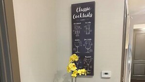 A bar area with two black leather barstools and a small round table, a blackboard with classic cocktails written on it, and a yellow orchid decoration. - High Rise Condo/Apartment in the Medical Center Area (Houston)