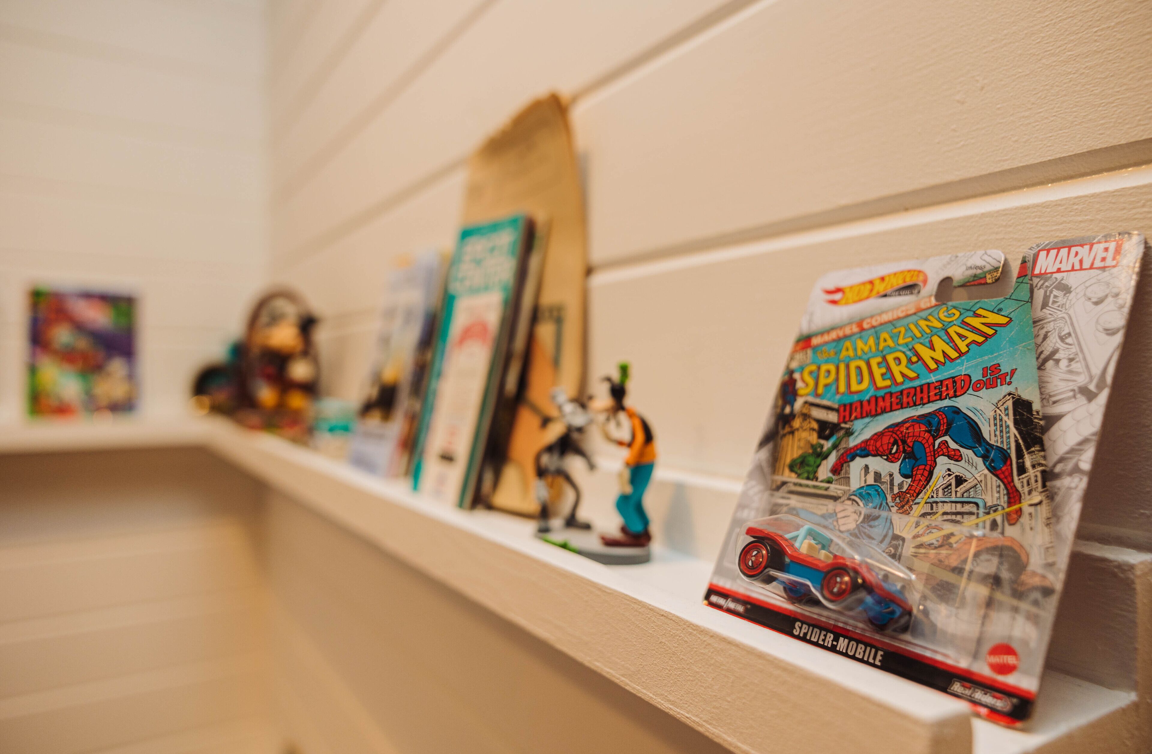 Uma estante com vários livros em quadrinhos e bonecos do Homem-Aranha.