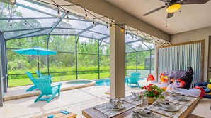 Un área de comedor al aire libre techada, con piscina, sillas y una mesa lista para una comida.