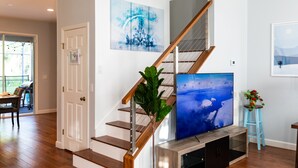 Una escalera con escalones de madera y barandilla metálica, un televisor de pantalla plana grande montado sobre un mueble de madera, y dos obras de arte enmarcadas en las paredes.