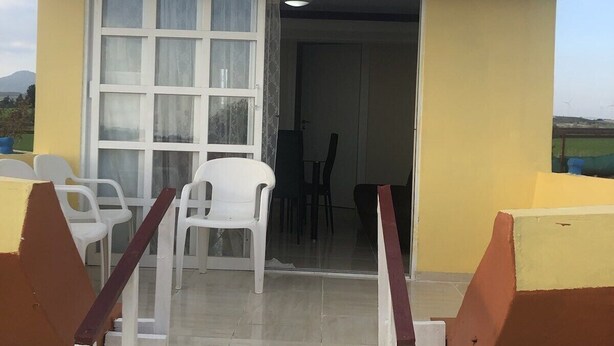 A small building with a yellow exterior, a door with glass panels, and a small outdoor seating area with white plastic chairs. - MERSINERA Paradise Garden NOAH  house (Trachoni)