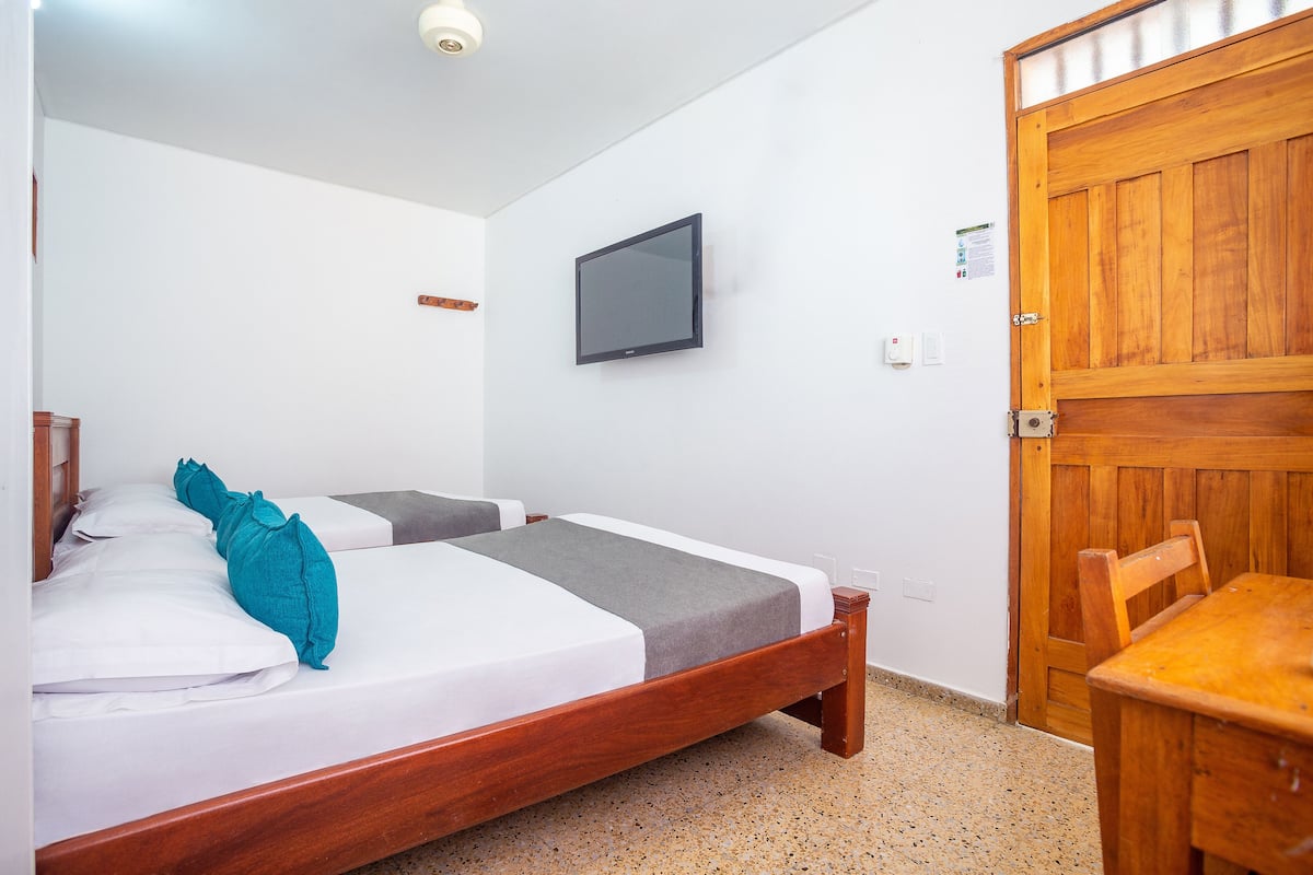 A bedroom with two beds, a wooden door, and a television on the wall.