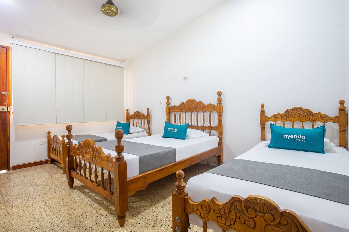 A hotel room with two wooden beds, each with a grey bedspread and a blue pillow labeled "ayenda HOTEL".