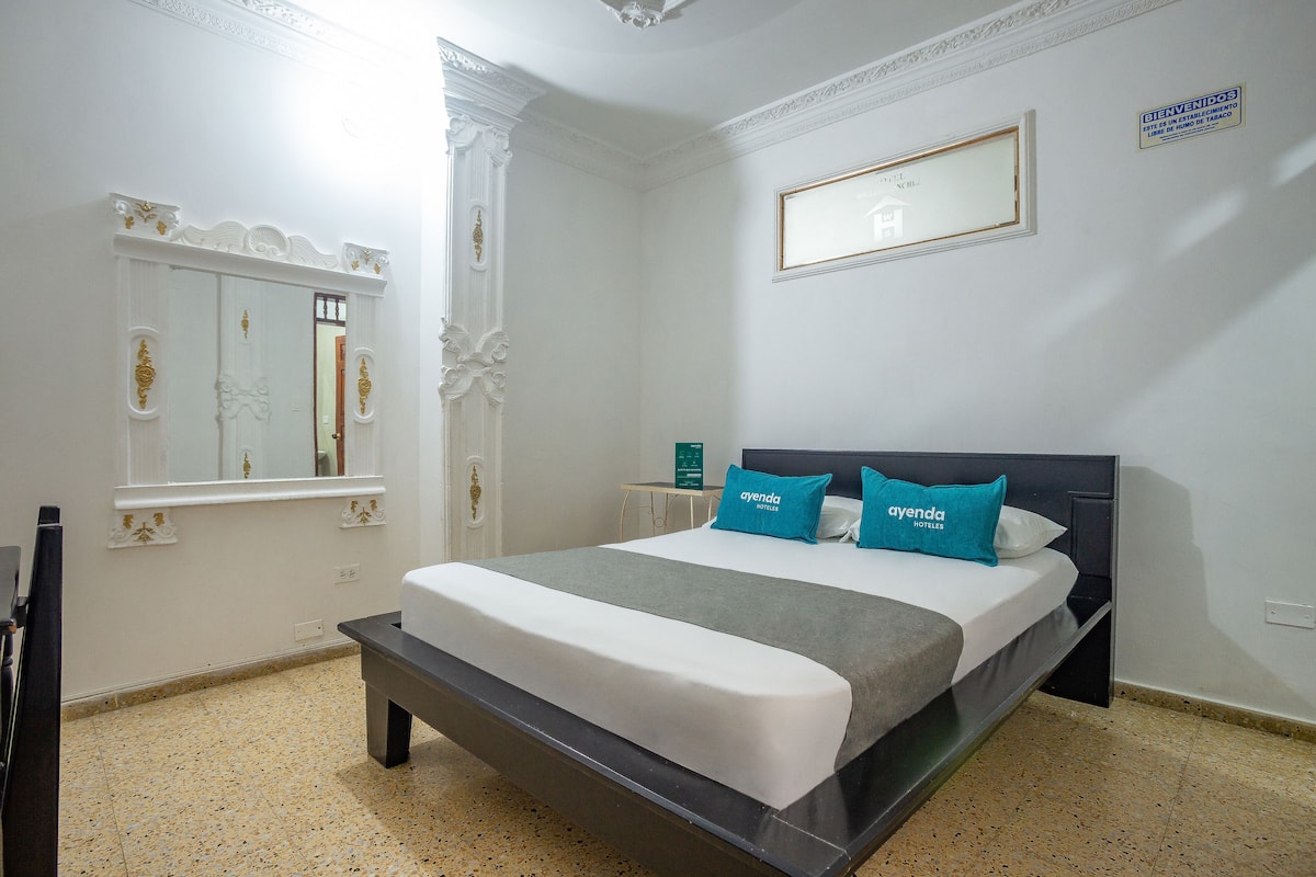 A hotel room with a large bed, a nightstand, a mirror, and a sign indicating the room number.