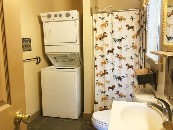 A compact bathroom with a white washing machine, a shower curtain with horse prints, and a sink with a mirror above it.