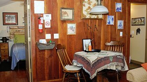 Une pièce chaleureuse aux murs en bois, une table à manger recouverte d’une nappe à motifs, une chaise en bois, ainsi que divers tableaux et affiches encadrés accrochés aux murs.