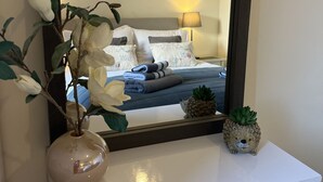 Une chambre à coucher comprenant un lit, une table de chevet, une lampe, un miroir, une commode et une plante.