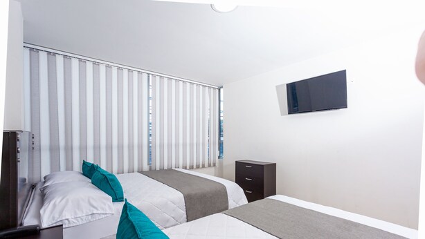 Een hotelkamer met twee bedden, een aan de muur bevestigde televisie en een raam met zonwering.