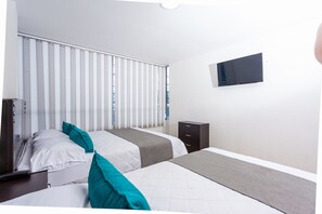 Ein Hotelzimmer mit zwei Betten, einem an der Wand befestigten Fernseher und einem Fenster mit Jalousien.