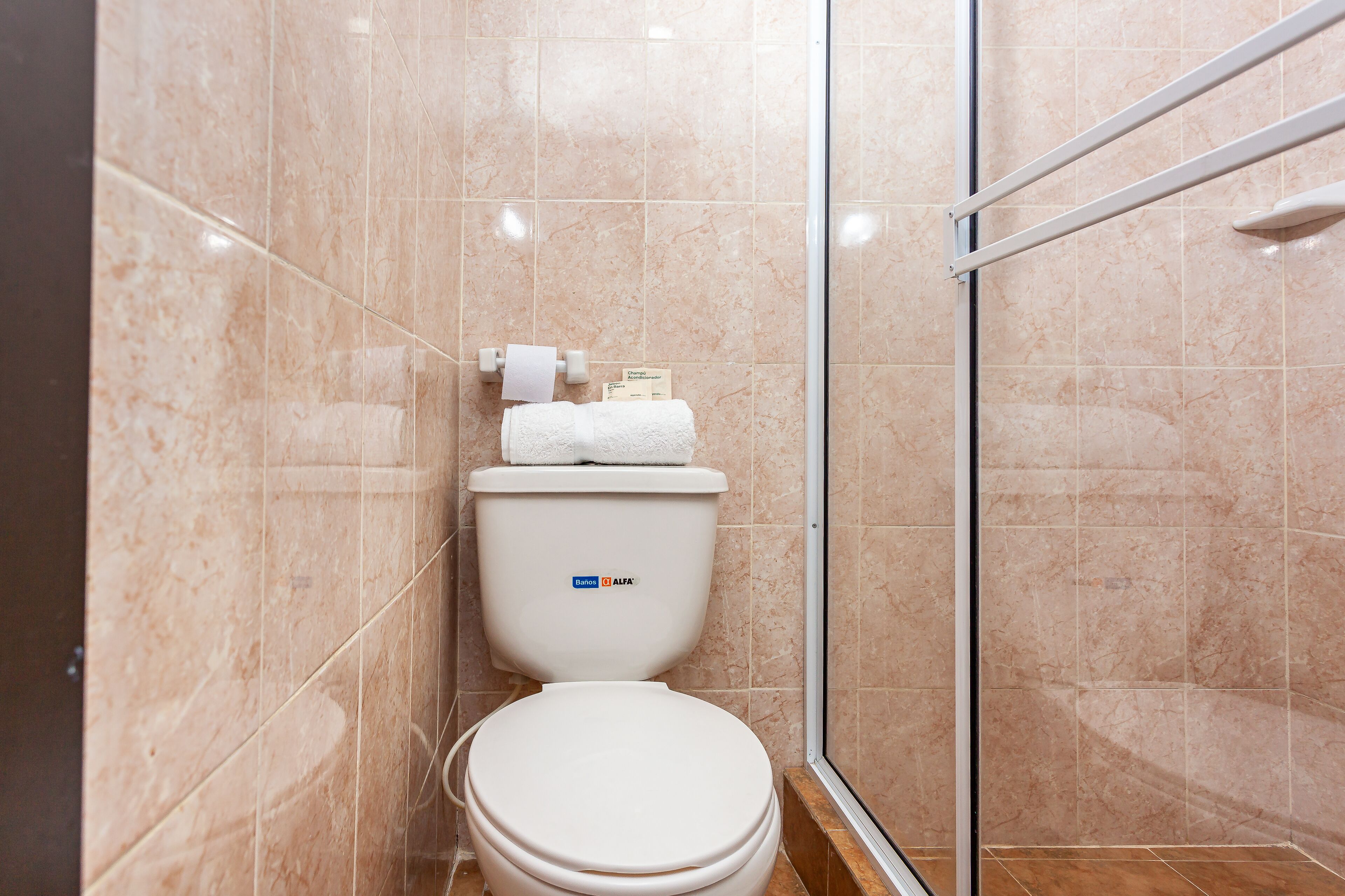 A modern bathroom with a toilet, a glass shower enclosure, and beige marble tiles.
