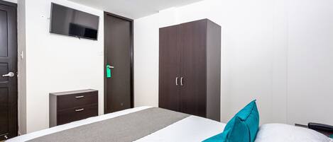A hotel room with a bed, a TV mounted on the wall, a wardrobe, and a small bedside table.