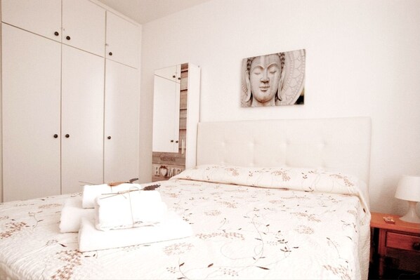 A bedroom with a large bed, a wardrobe, a mirror, and a wall-mounted artwork.