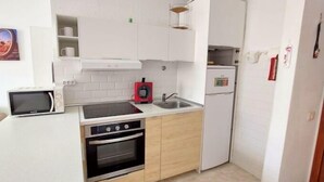 A compact kitchen with white cabinets, a microwave, a stove, and a refrigerator. - Centrally located on the beachfront in Los Cristianos (Arona)