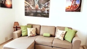 A L-shaped sectional sofa with multiple cushions, a lamp, and three framed pictures on the wall. - Centrally located on the beachfront in Los Cristianos (Arona)