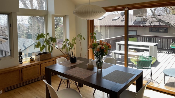 Un comedor con una mesa de madera, sillas y un jarrón de flores. Hay ventanas grandes y vistas al exterior.