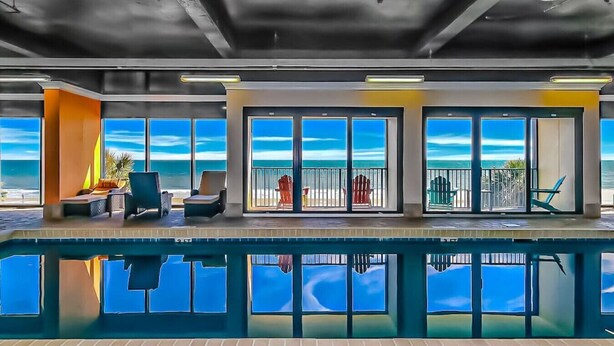 Ein Poolbereich mit Meerblick, Liegestühlen und einem verglasten Balkon.