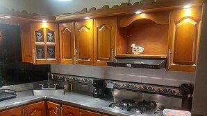 Une cuisine avec des meubles de rangement en bois, une cuisinière à gaz et un luminaire suspendu.