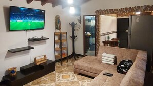 Un salon avec un grand canapé marron, un téléviseur à écran plat fixé au mur, un plafond en bois et un sol carrelé.