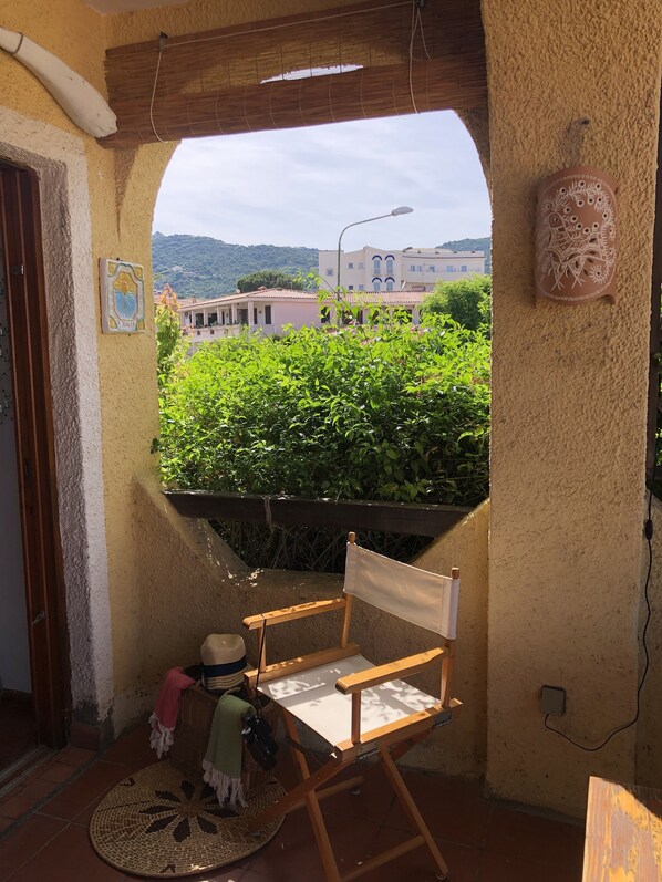 A small balcony with a wooden chair, a woven mat, and a decorative wall piece.