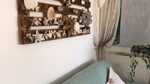 A room with a wooden wall art piece displaying various seashells and starfish, a green sofa with patterned cushions, and a window with curtains. - Casa Maria Pia, relaxation and sea in the heart of Cannigione (Cannigione)