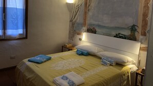A bedroom with a bed, a nightstand, a wall-mounted lamp, and a window with curtains. - Casa Maria Pia, relaxation and sea in the heart of Cannigione (Cannigione)