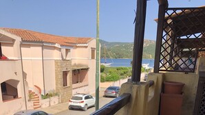 A balcony with a view of a street, a building with a tiled roof, and a body of water in the distance. - Casa Maria Pia, relaxation and sea in the heart of Cannigione (Cannigione)