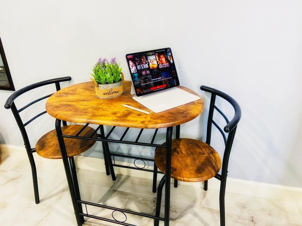 A round wooden table with a laptop displaying a music video, a small potted plant, and a notebook.
