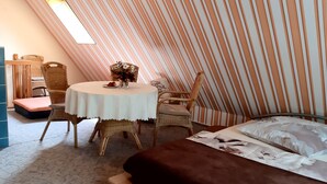 Een gezellige kamer met een bed, een ronde tafel met stoelen, een bijzettafeltje met bloemen en een gestreepte wand.