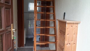 Een houten ladder die leidt naar een hoger gelegen gedeelte, een houten kast en een deur met sleutelslot.