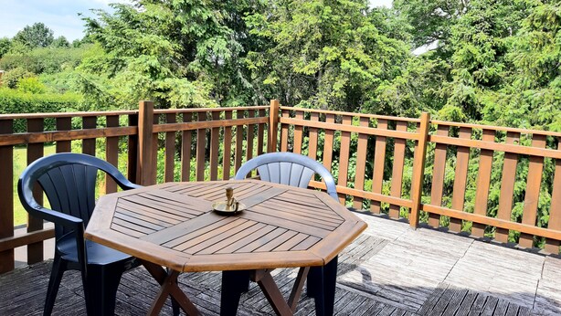 Een houten terras met een ronde tafel en twee stoelen, omgeven door een houten leuning.