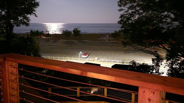 Vista notturna da un pontile di legno su una spiaggia con mare calmo e una luna luminosa nel cielo.
