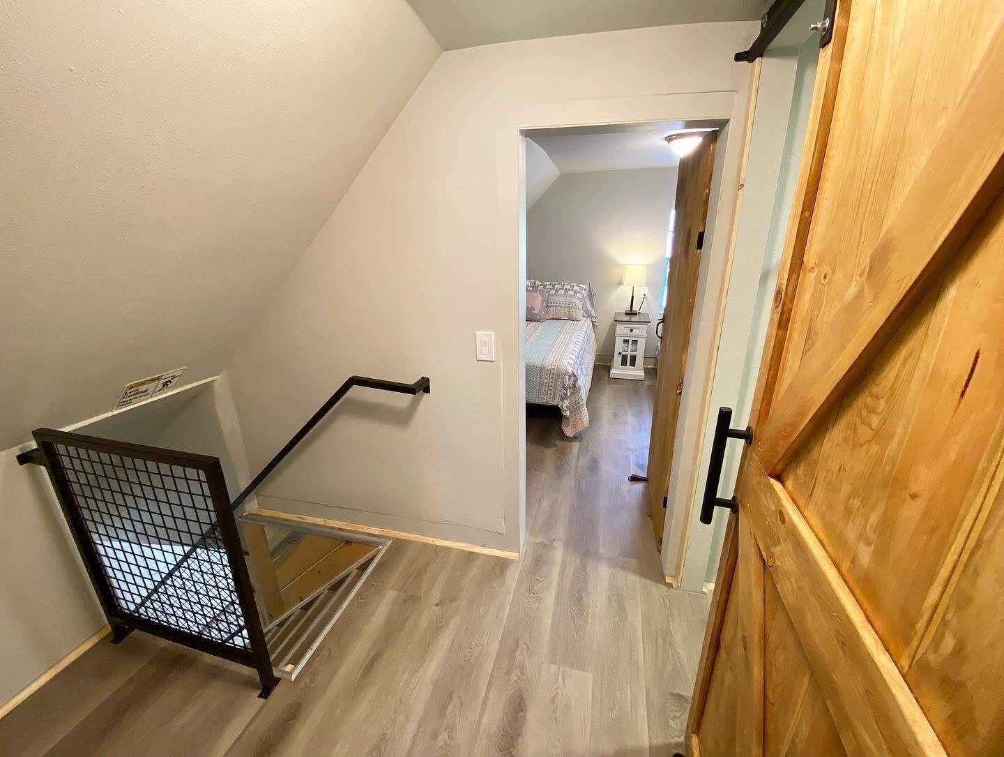 A staircase with a metal handrail leading to a bedroom with a bed and nightstand.