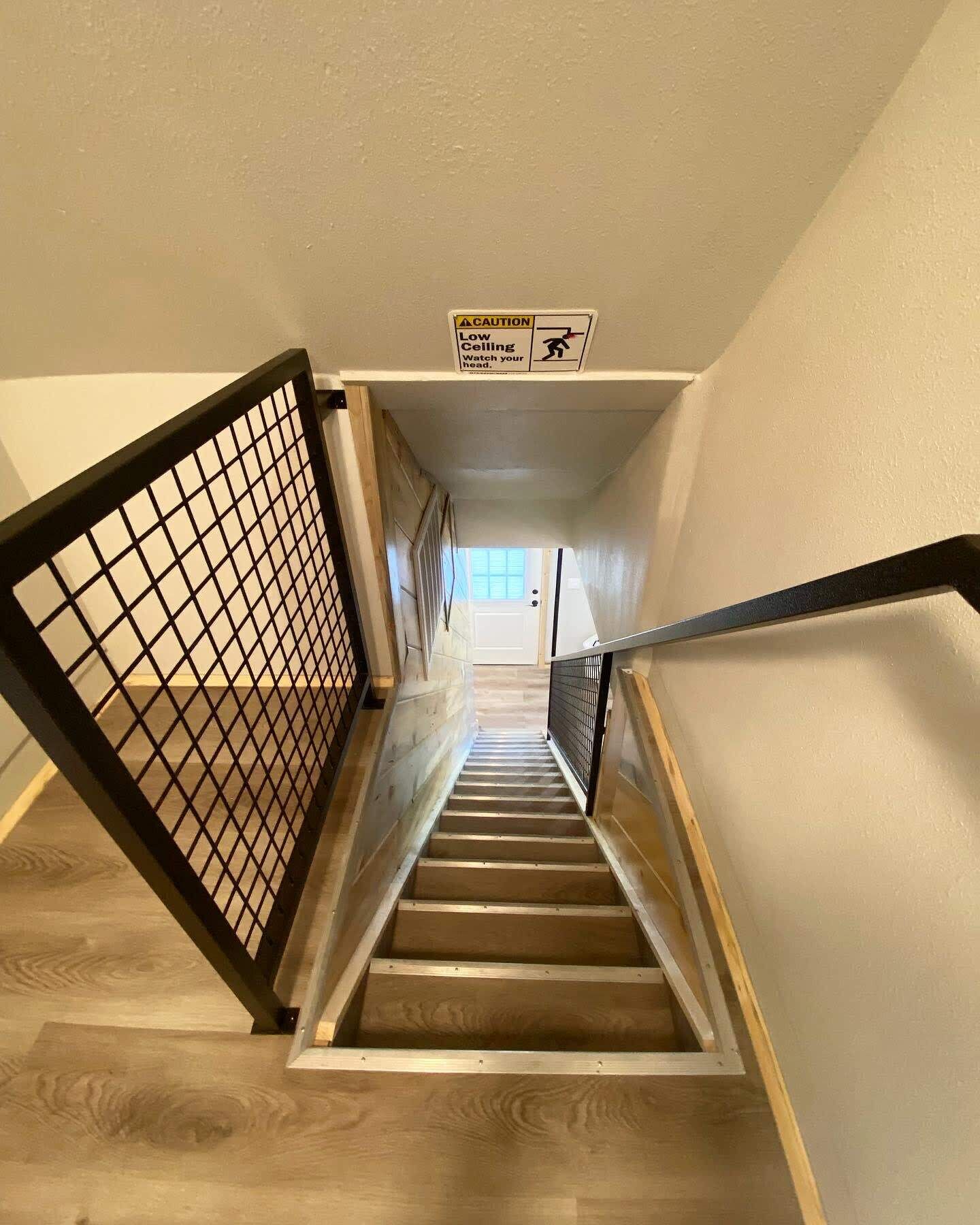 A staircase with a caution sign for a low ceiling, wooden steps, and a metal handrail.