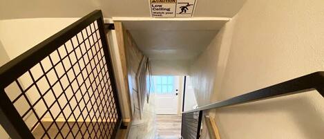 A staircase with a caution sign for a low ceiling, wooden steps, and a metal handrail.