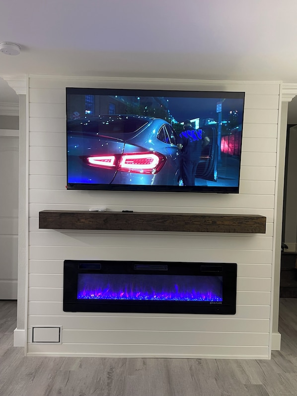 A flat-screen TV mounted on a white wall with a wooden shelf below.