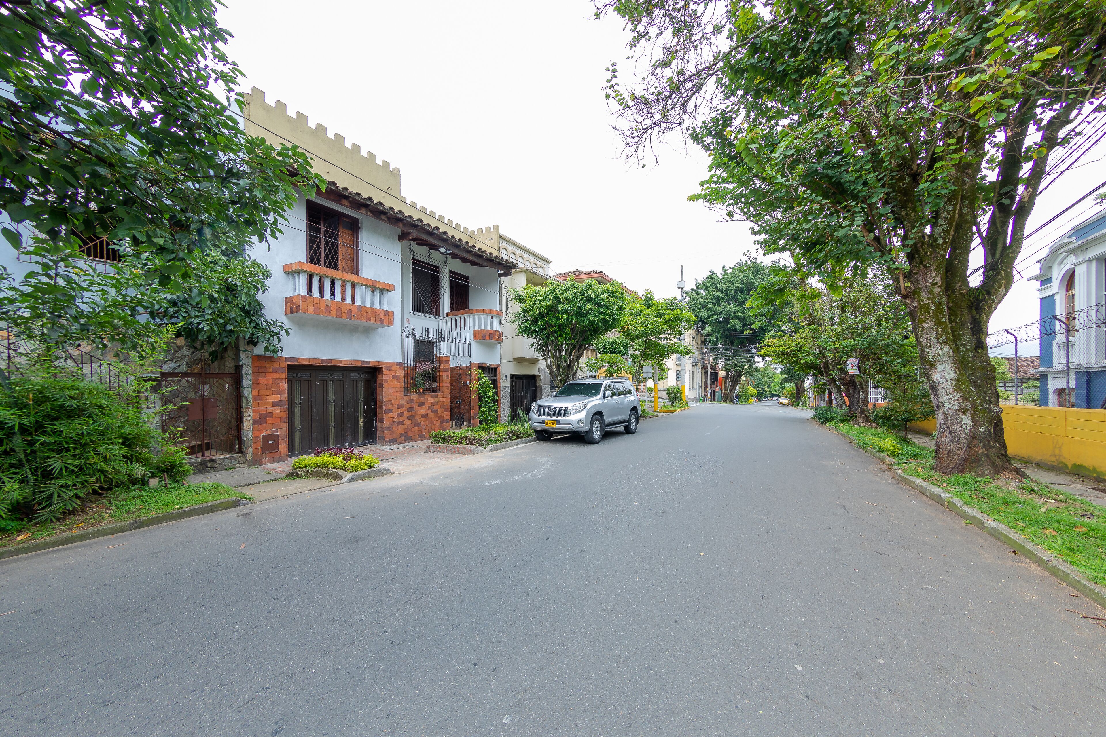 Una calle flanqueada por edificios residenciales, un SUV estacionado y árboles.