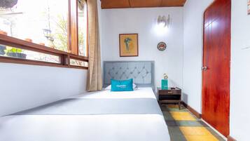 A hotel room with a bed, a nightstand, a wooden door, and a window with curtains.