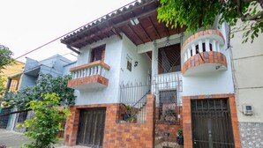 Ein zweistöckiges Haus mit Balkon, geschlossenem Eingangstor und einem kleinen Garten.