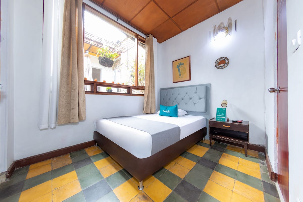 Un dormitorio con cama, mesita de noche, ventana con cortinas y suelo estampado.