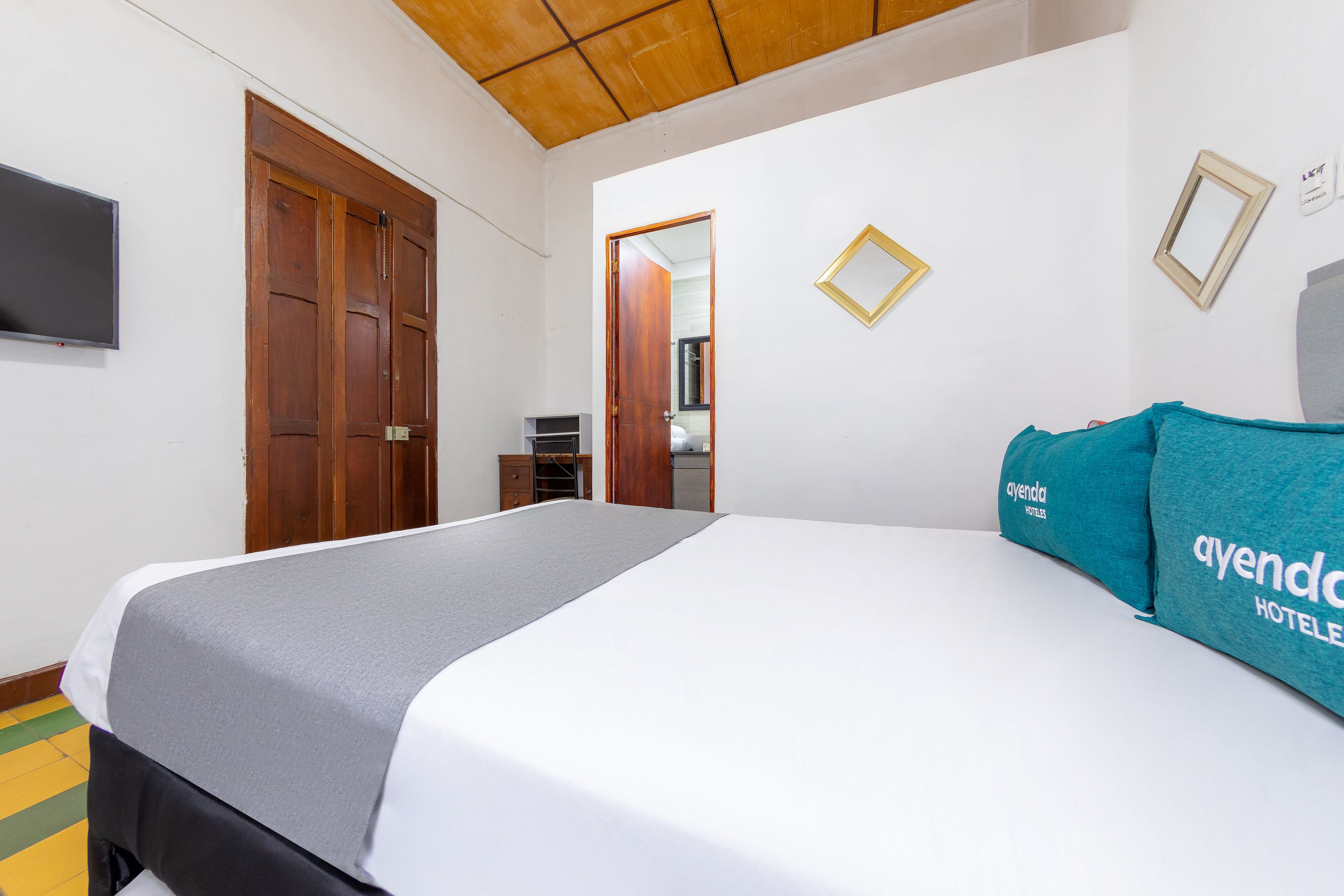 A hotel room with a bed, a TV, wooden doors, and a small desk.