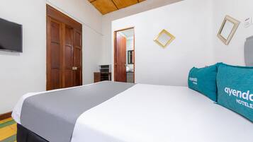 A hotel room with a bed, a TV, wooden doors, and a small desk.